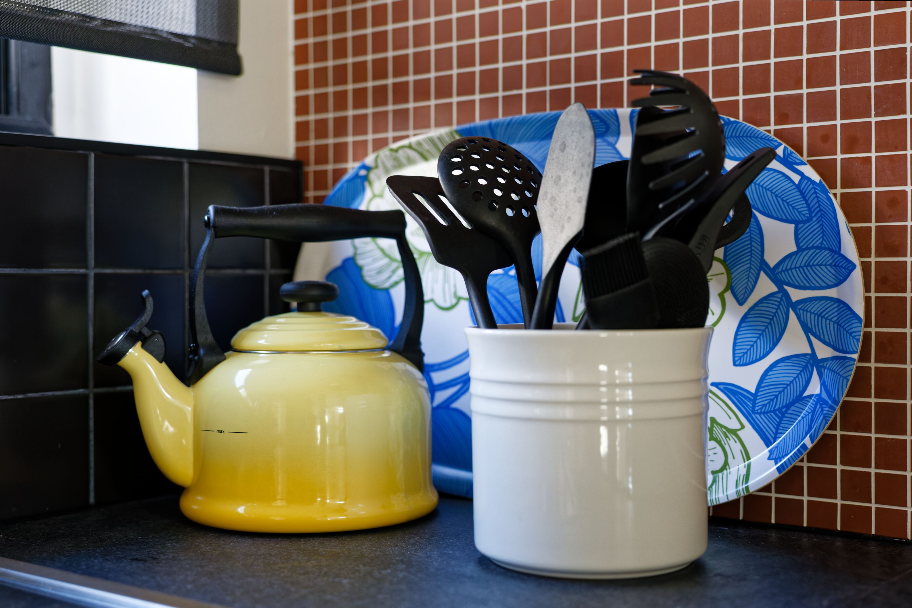 Un comptoir de cuisine avec une théière jaune, une tasse blanche et une assiette bleue ornée d’un motif de feuilles.