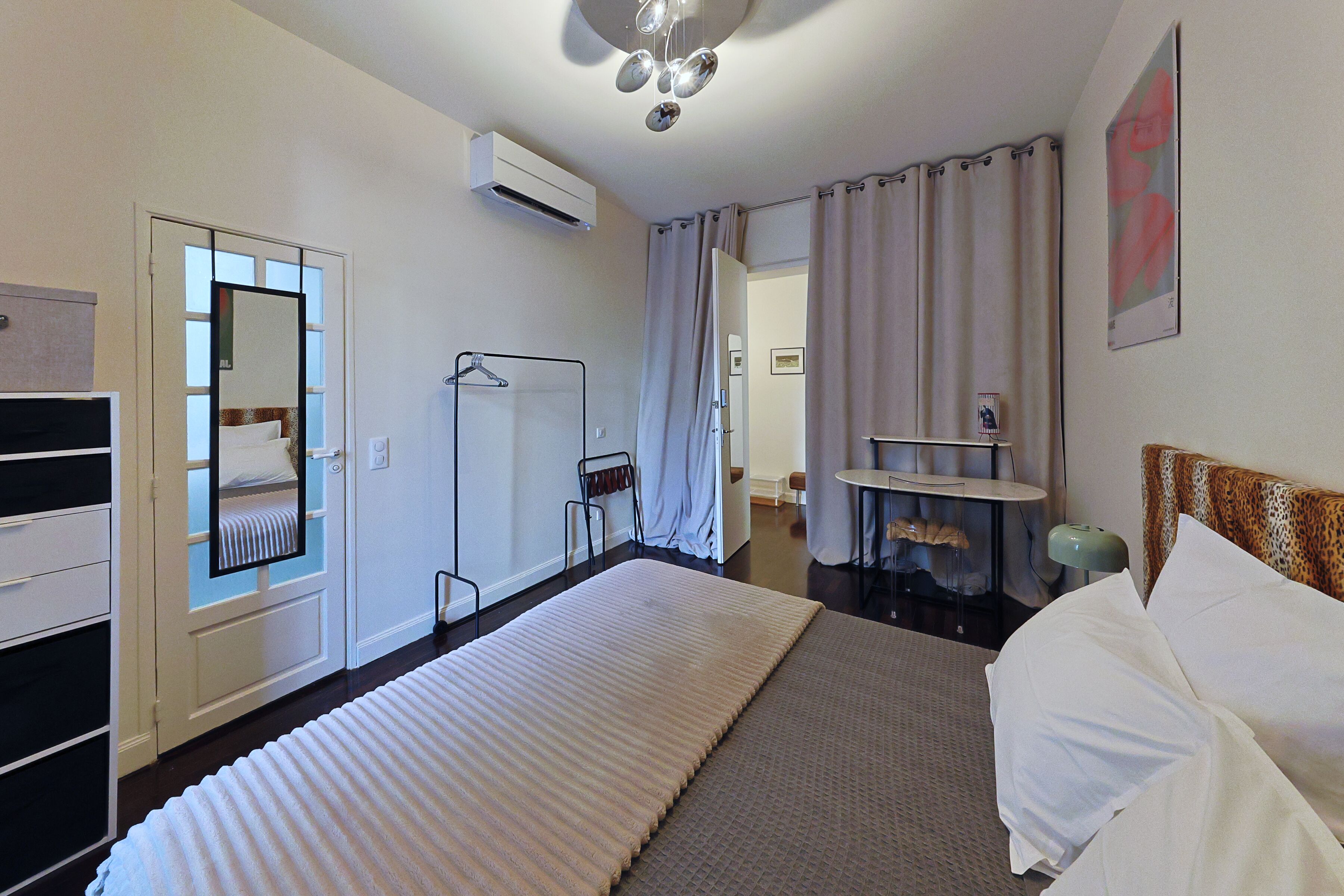 A hotel room with a bed, a desk, a mirror, and a bathroom visible through an open door.