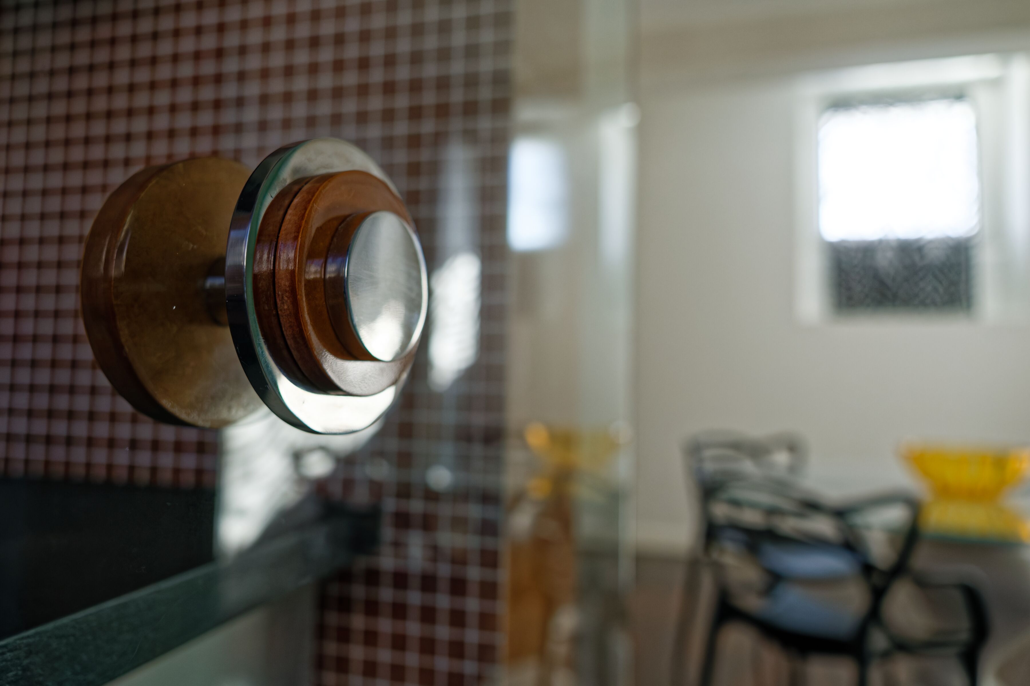 A close-up of a door handle with a metallic and wooden design, set against a checkered wall.