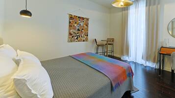 Een hotelkamer met een bed, een bureau, een stoel, een hanglamp en een raam met gordijnen.