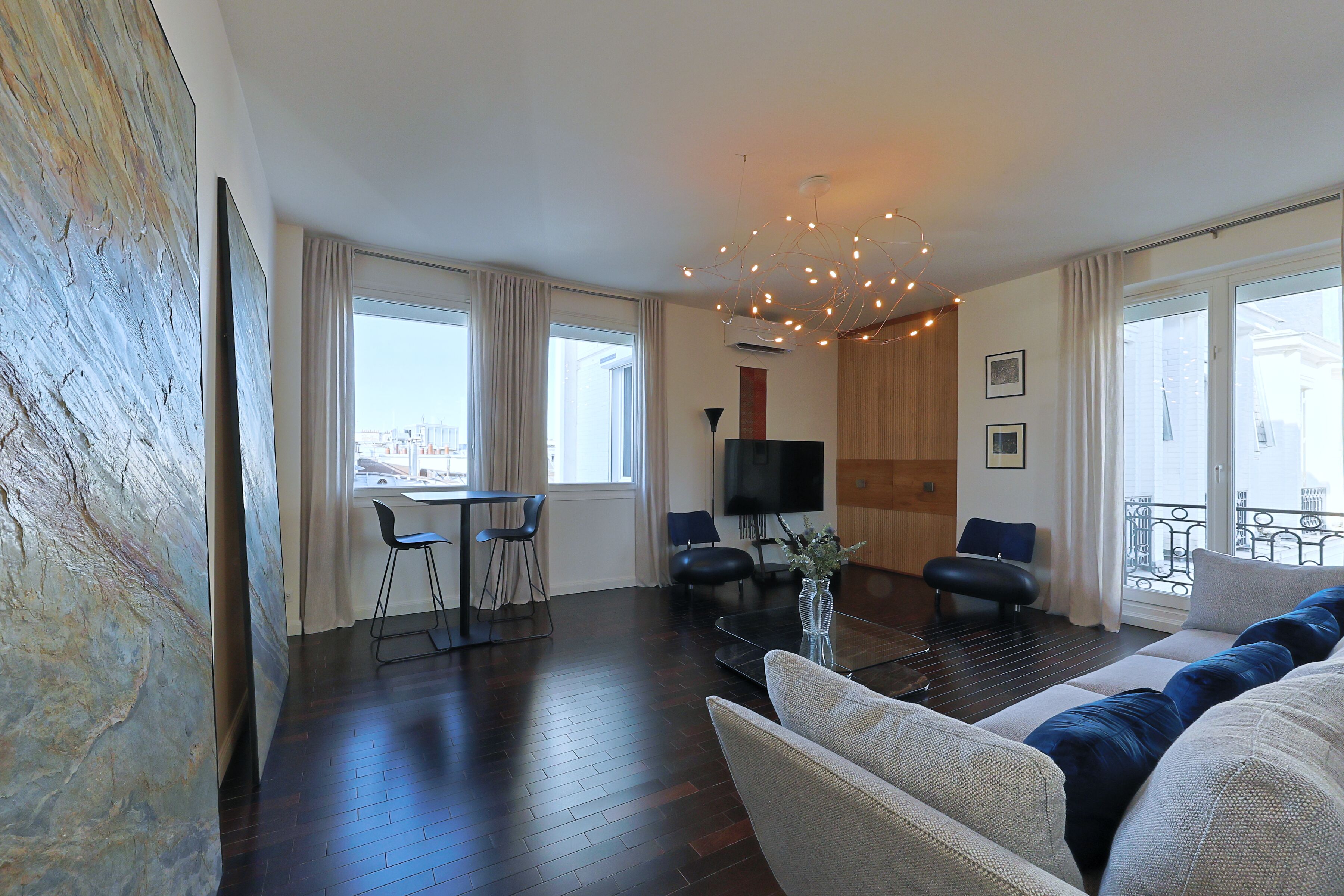 Un salon moderne avec un parquet en bois foncé, un canapé, deux fauteuils, une table basse et un téléviseur.