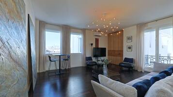 Een moderne woonkamer met een donker houten vloer, een bank, twee fauteuils, een salontafel en een televisie.