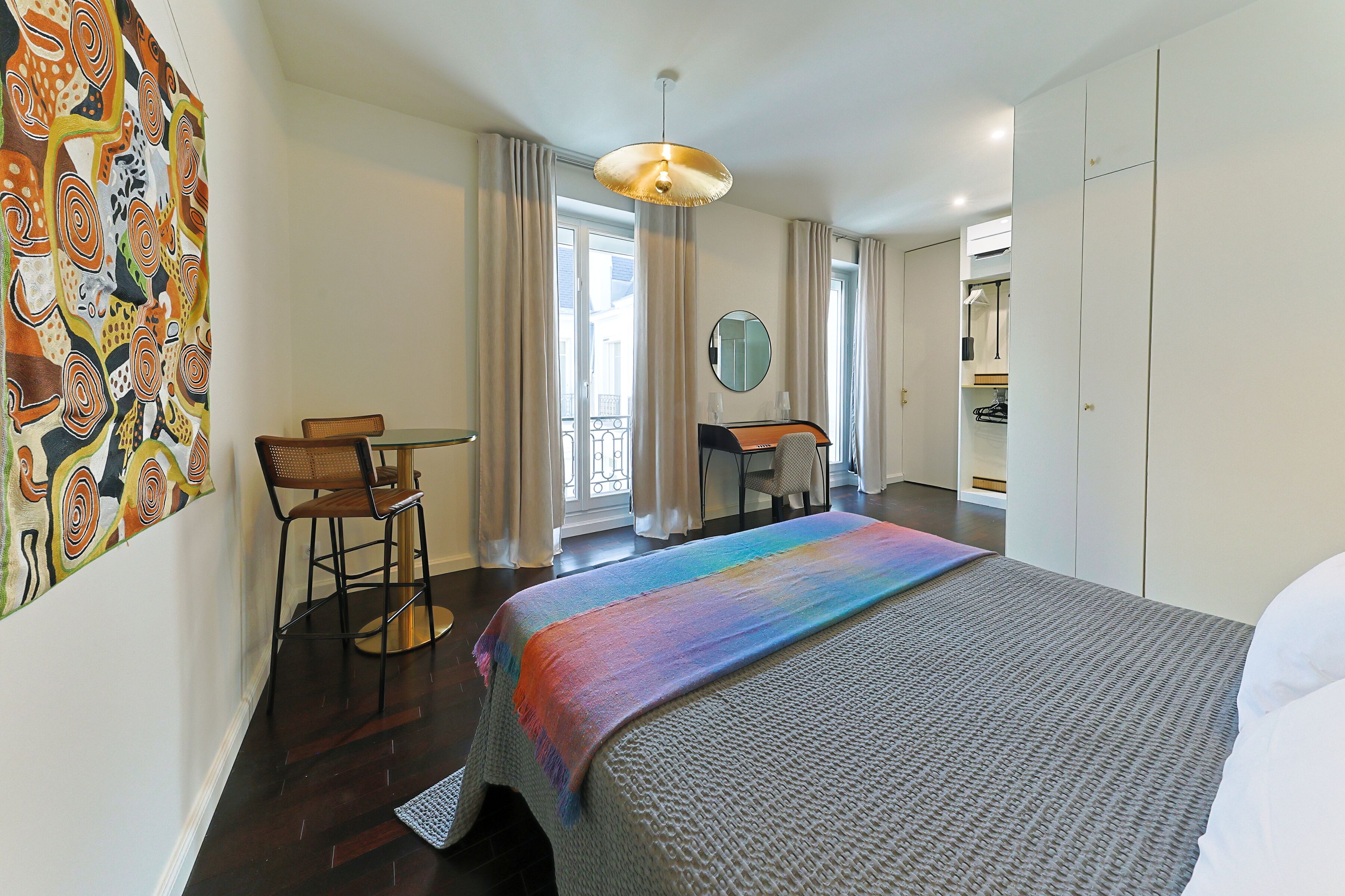 A hotel room with a bed, a desk, a chair, a mirror, and a window.
