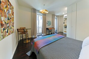 A hotel room with a bed, a desk, a chair, a mirror, and a window.