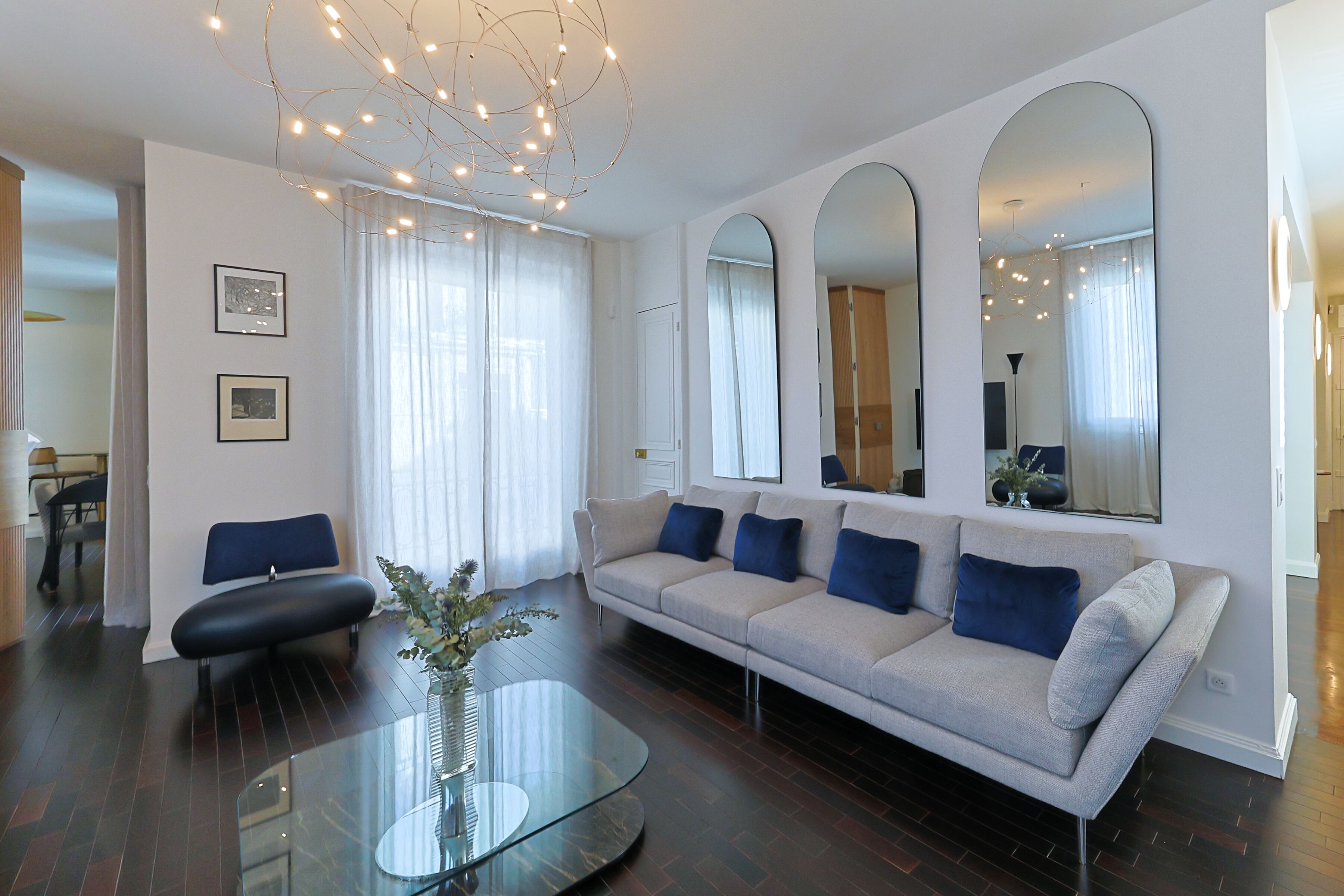 A modern living room with a sofa, a glass coffee table, and a dining area in the background.