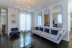 A modern living room with a sofa, a glass coffee table, and a dining area in the background.