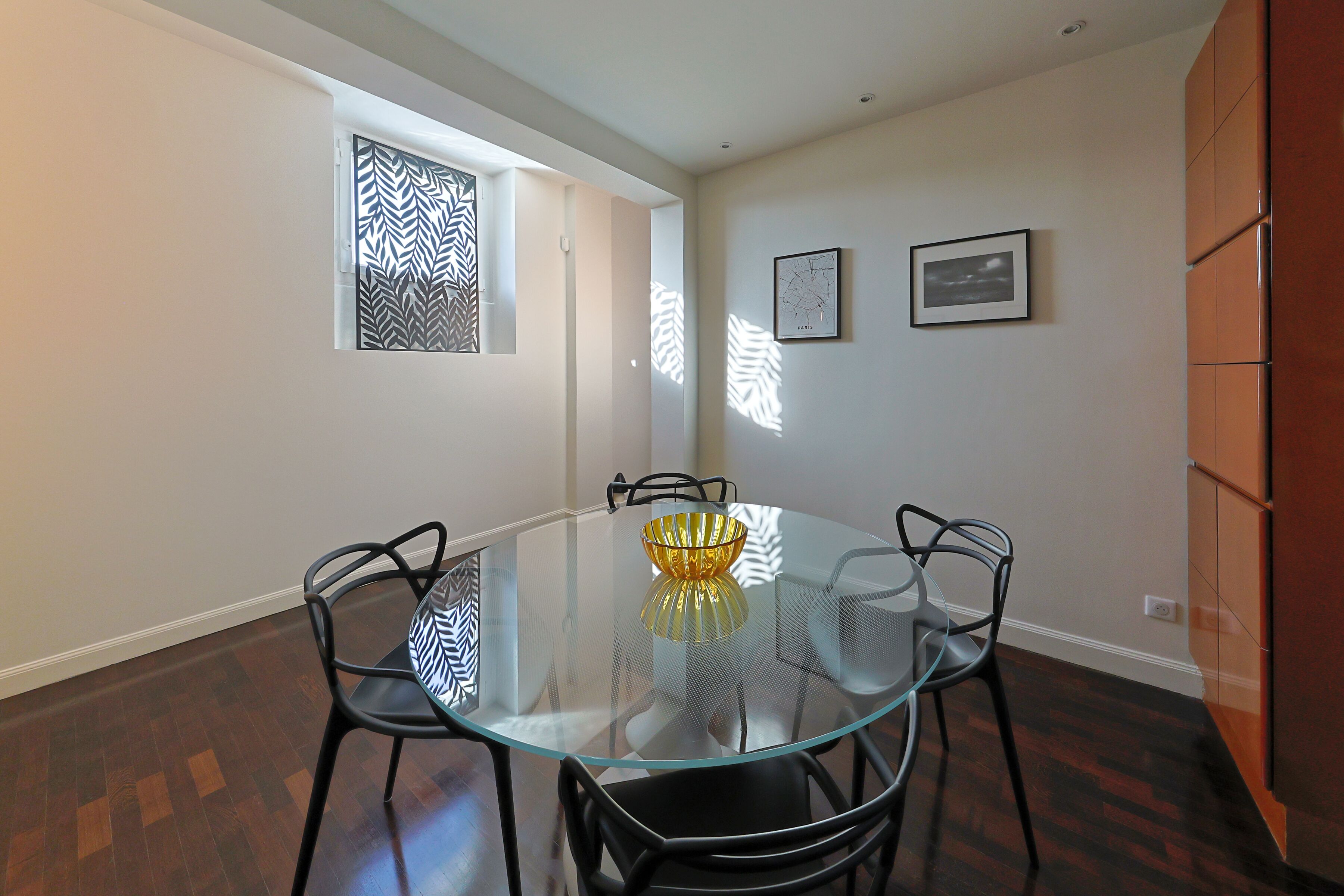 Un coin repas avec une table et des chaises en verre, un bol décoratif et deux tableaux encadrés accrochés au mur.