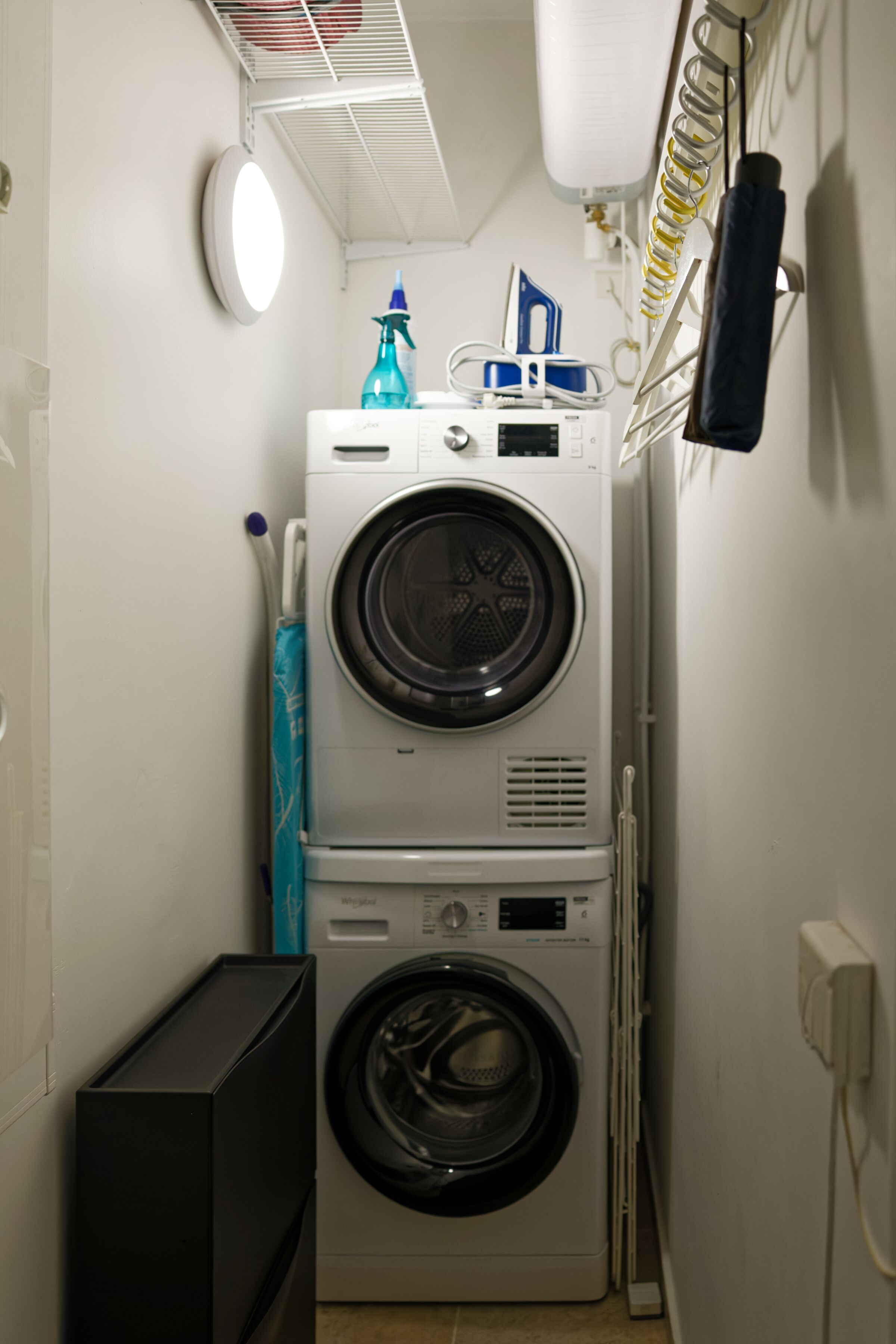 Een ruimtelijk wasgedeelte met gestapelde wasmachines en drogers, een droogrek en een klein kastje.