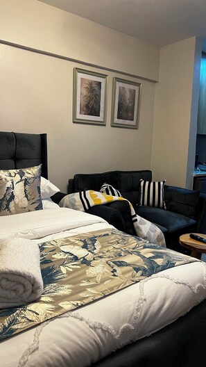 A hotel room with a bed, two armchairs, a small table, and two framed pictures on the wall.
