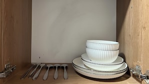 A wooden cabinet with a white interior, containing stacked white bowls and a set of silver spoons. - Step into effortless luxury at The Mesquite Studio. (Nairobi)