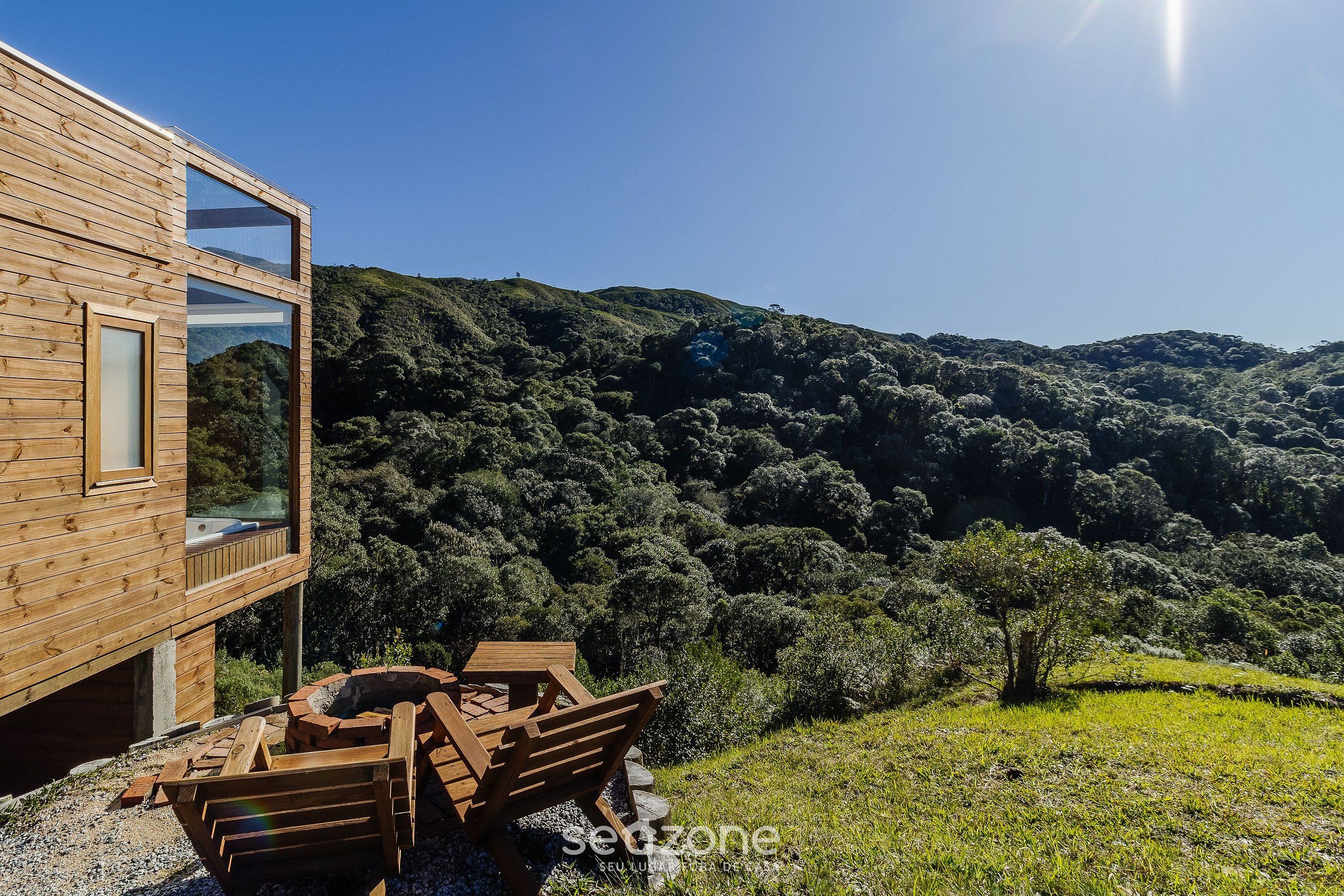 A wooden cabin with large windows overlooking a forested hillside.
