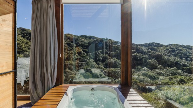 Un bain à remous avec une terrasse en bois et une vue sur une colline boisée.