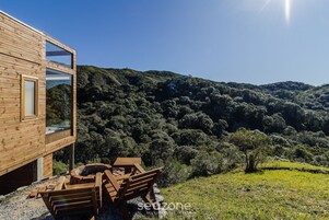 Una cabaña de madera con amplias ventanas que dan a una ladera boscosa.
