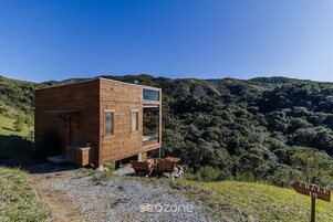 Una cabaña de madera con una pequeña terraza, rodeada por un paisaje boscoso.