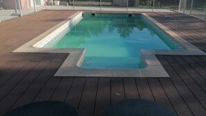 Une piscine rectangulaire dont les bords sont recouverts de carreaux, entourée d’une terrasse en bois.
