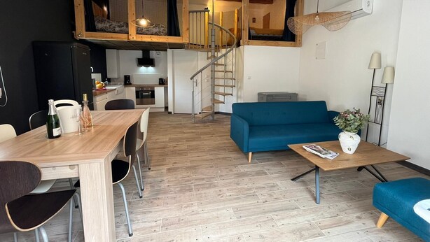 Un espace de vie moderne comprenant un coin repas, un canapé bleu et un escalier menant à un niveau supérieur.