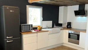 Une cuisine compacte équipée d’un réfrigérateur noir, d’un four à micro-ondes, d’un évier avec un égouttoir, d’une machine à café et d’un four encastré.