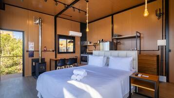 A modern bedroom with a large bed, a desk, and a kitchenette.