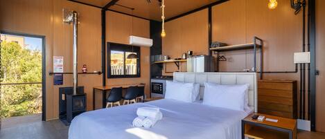 A modern bedroom with a large bed, a desk, and a kitchenette.