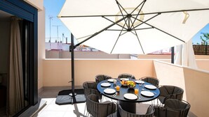 Un balcón con una mesa redonda dispuesta para comer, rodeado de sillas y protegido por un gran paraguas.