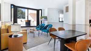Una sala de estar moderna con un sofá, una mesa de centro y un televisor. Hay un balcón con vistas a árboles y una motocicleta.