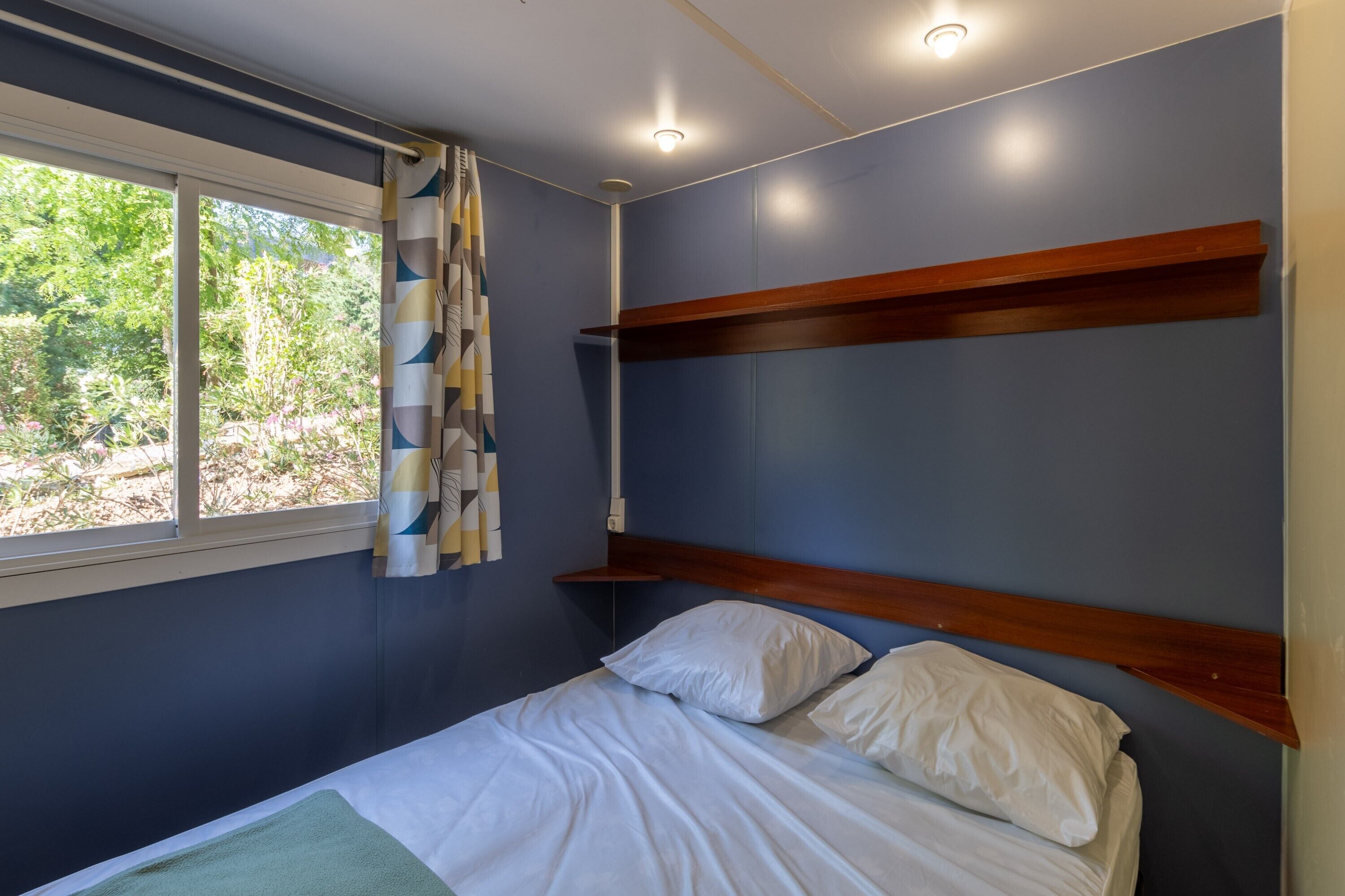 Un dormitorio con cama, ventana con cortinas, cabecero de madera y luz en el techo.