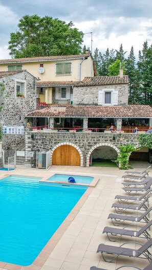 A stone building with a swimming pool and lounge chairs.