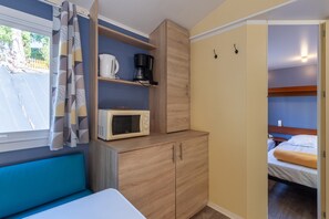 Een kleine kamer met een bed, een magnetron, een koffiezetapparaat en een kast.