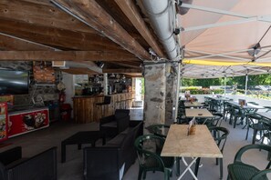 Un café en plein air avec des poutres en bois, des piliers en pierre et des chaises en plastique vertes.