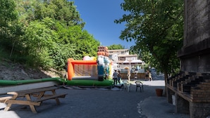 An outdoor area with a large inflatable structure, picnic tables, and a brick wall. - Mobile Home 'Mobil-home E - 1-6 Pers' with Shared Pool, Private Terrace and Shared Garden (Lavilledieu)