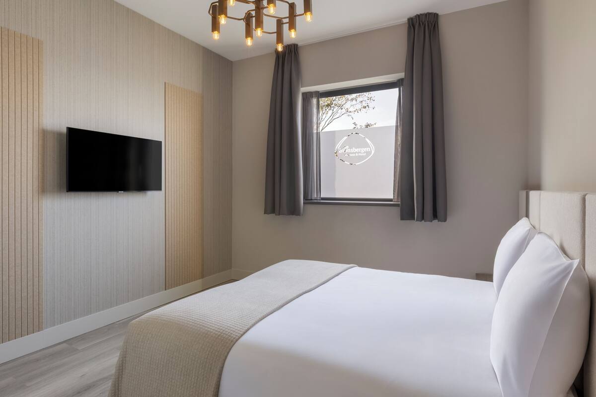 A modern hotel room with a flat-screen TV mounted on the wall, a large bed with white linens, and a window with curtains.