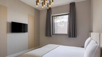 A modern hotel room with a flat-screen TV mounted on the wall, a large bed with white linens, and a window with curtains.