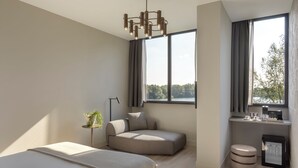 Un dormitorio moderno con una cama, un sofá, una mesita con una planta, un escritorio con una cafetera y un ventanal con cortinas.