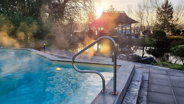 Una piscina con barandilla de metal, rodeada por un patio de piedra y una masa de agua que refleja el sol.