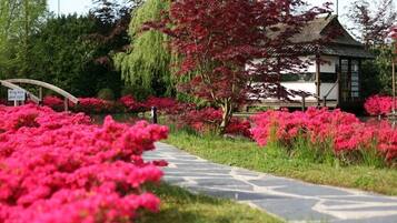 Un camino bordeado de flores rosadas, un edificio de estilo tradicional y un letrero que indica un estacionamiento.