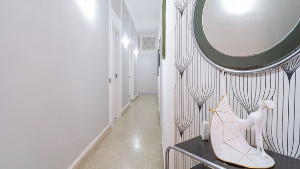 Un pasillo con paredes blancas, piso de baldosas y un espejo con marco decorativo.