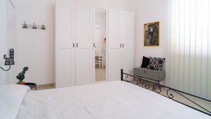 Un dormitorio con una cama grande, un armario blanco y una mesita con un cactus.
