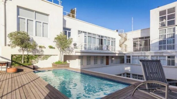 Un edificio moderno con piscina, terraza de madera y mobiliario exterior.