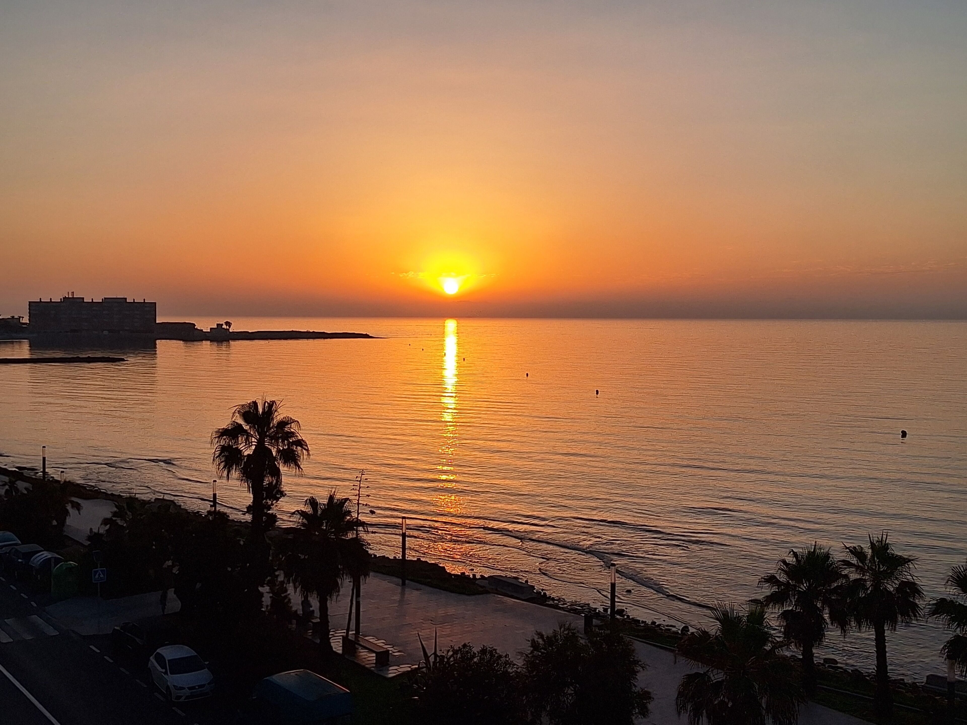 Un atardecer sobre un mar tranquilo con un edificio distante a la izquierda.