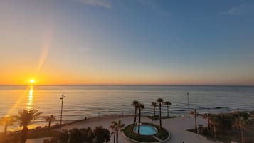Tramonto su un mare calmo, con una piscina e palme sullo sfondo.
