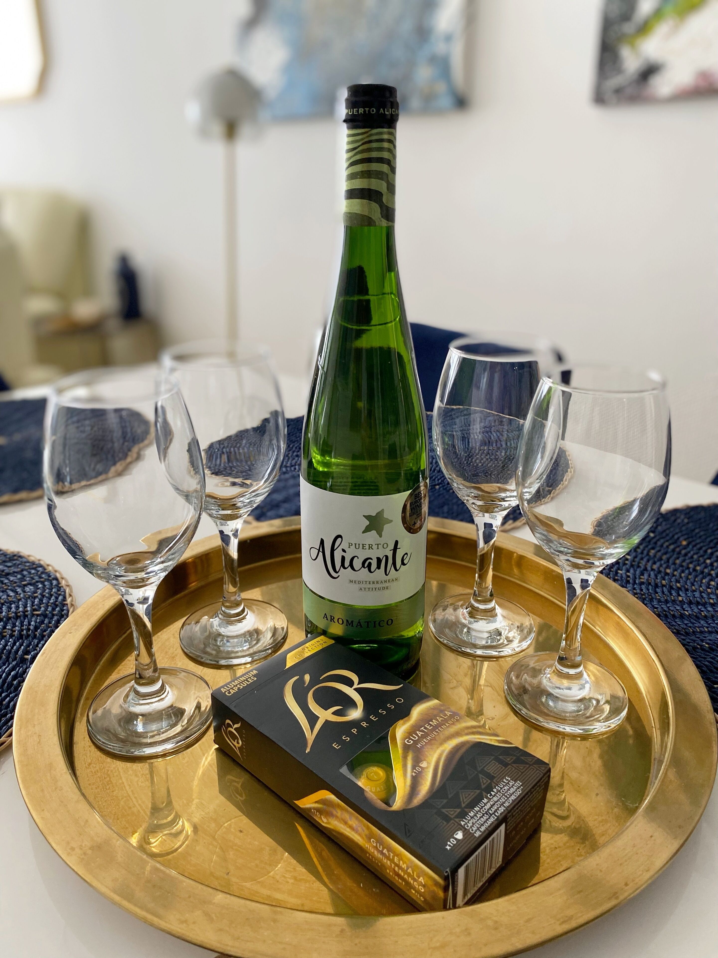 Una botella de vino de Puerto Alicante, cuatro copas de vino vacías y una caja de chocolate guatemalteco sobre una bandeja dorada.