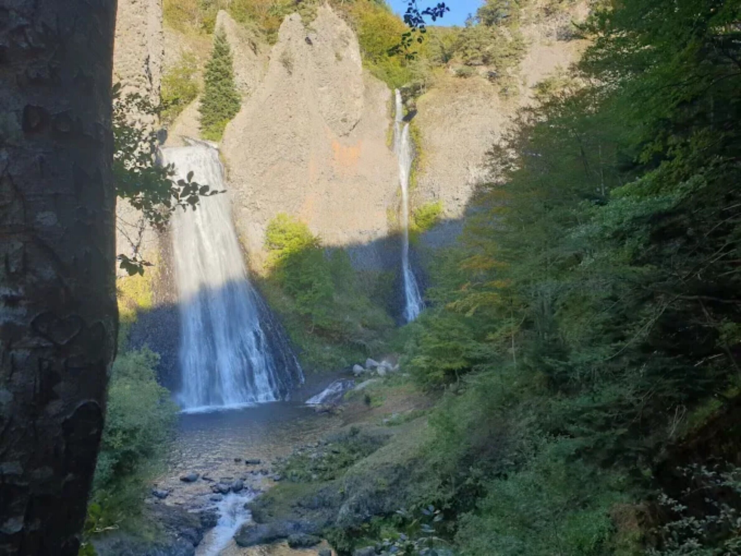 A natural waterfall surrounded by dense greenery and rocky terrain.