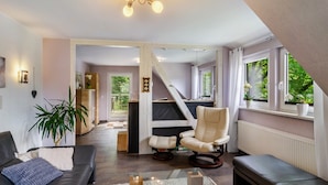 A modern living room with a sofa, armchair, and a glass coffee table. - Modern Apartment in Dream Location with Mountain View, Shared Garden and Wi-Fi (Langelsheim)