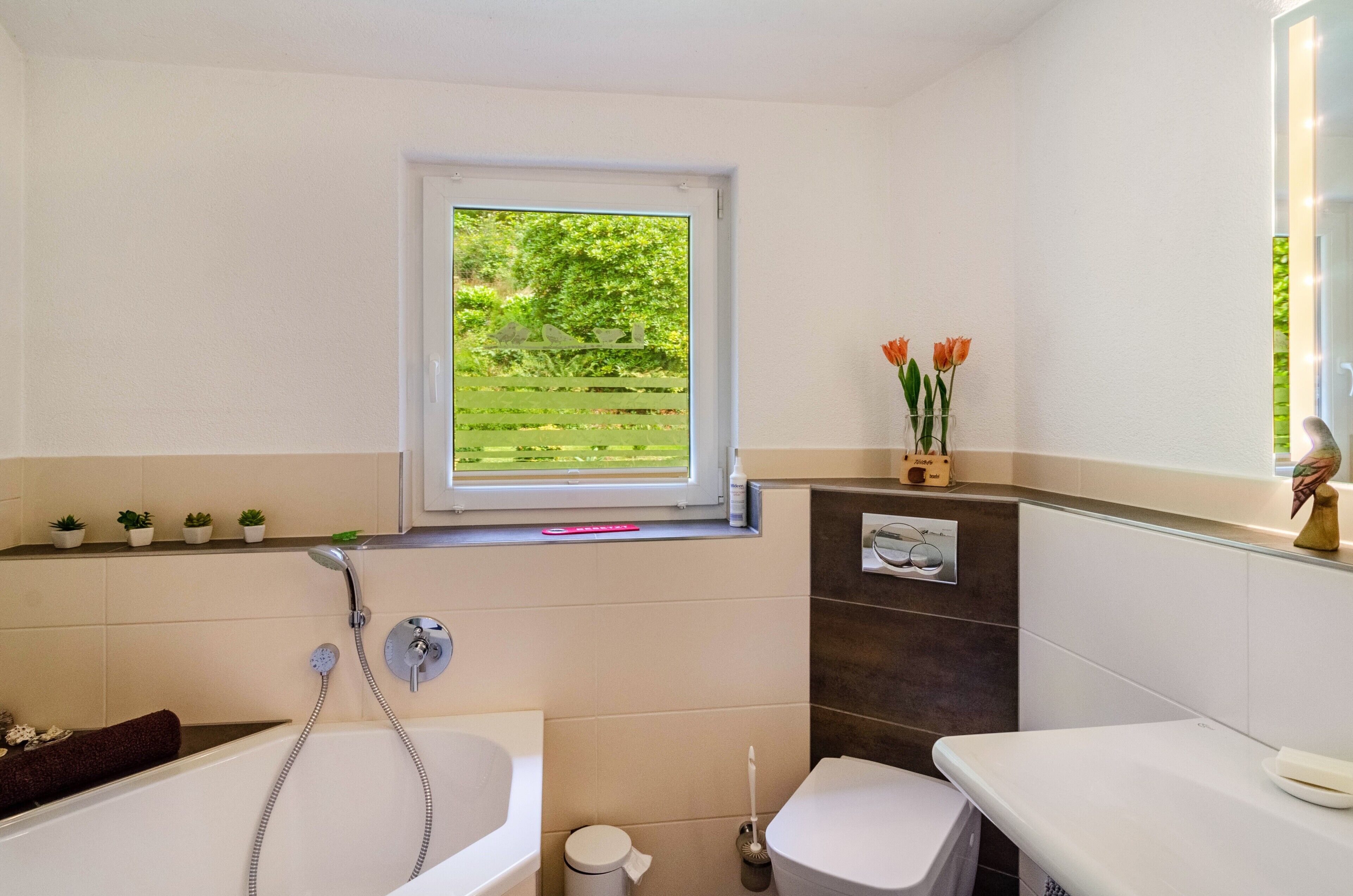 A bathroom with a bathtub, toilet, and window with a view of greenery.