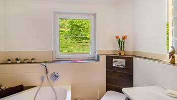 A bathroom with a bathtub, toilet, and window with a view of greenery.