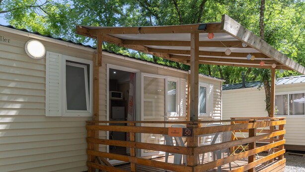 Une terrasse en bois avec un espace abrité, une pancarte indiquant « Saint-Stanislas 50 », et une fenêtre avec des stores.