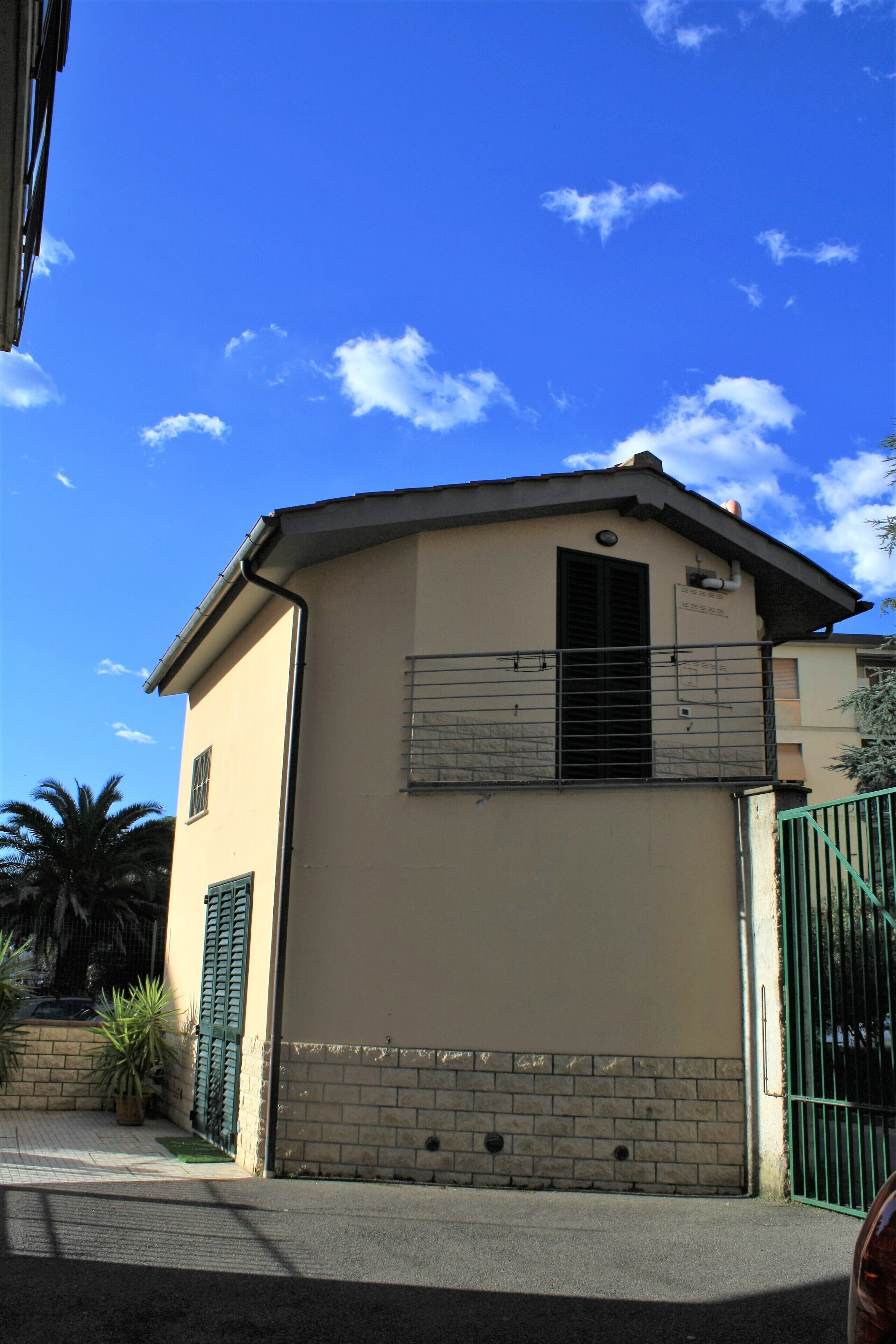 A two-story building with a beige facade, a balcony with metal railings, and a green gate.