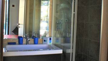 A bathroom with a glass shower enclosure, a double sink with a mirror above, and a towel rack.