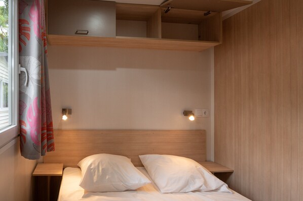 Una cama individual con ropa de cama blanca, cabecero de madera y dos lámparas de noche.