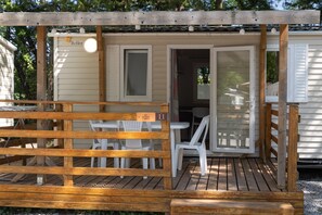 Una terraza de madera con zona de estar techada, una mesa y sillas.